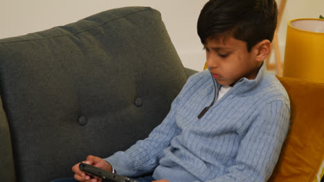 Young-Boy-Sitting-On-Sofa-At-Home-Playing-Game-Or-Streaming-Onto-Handheld-Gaming-Device-3